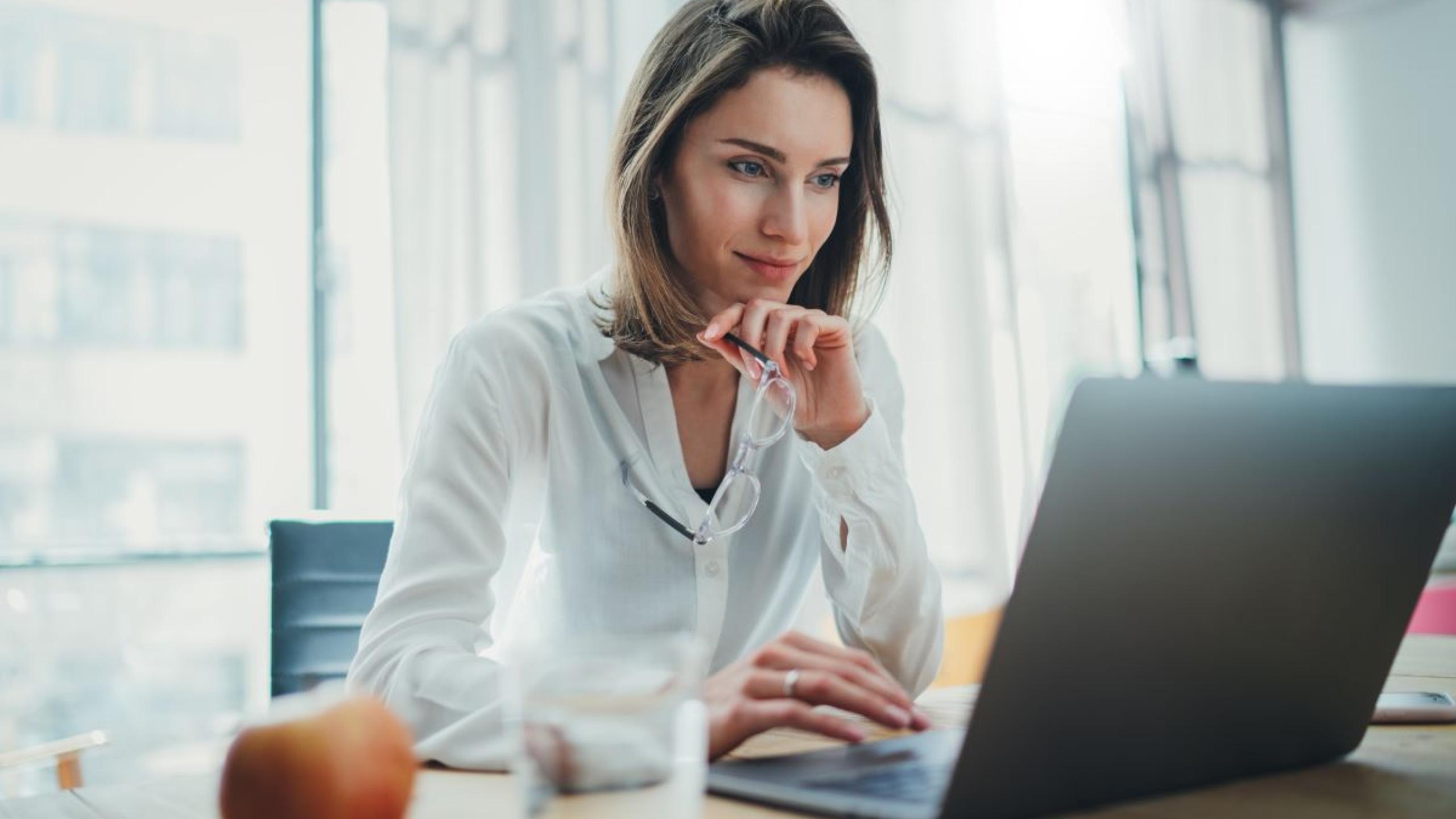 Vrouw aan bureau bekijkt scherm van laptop.