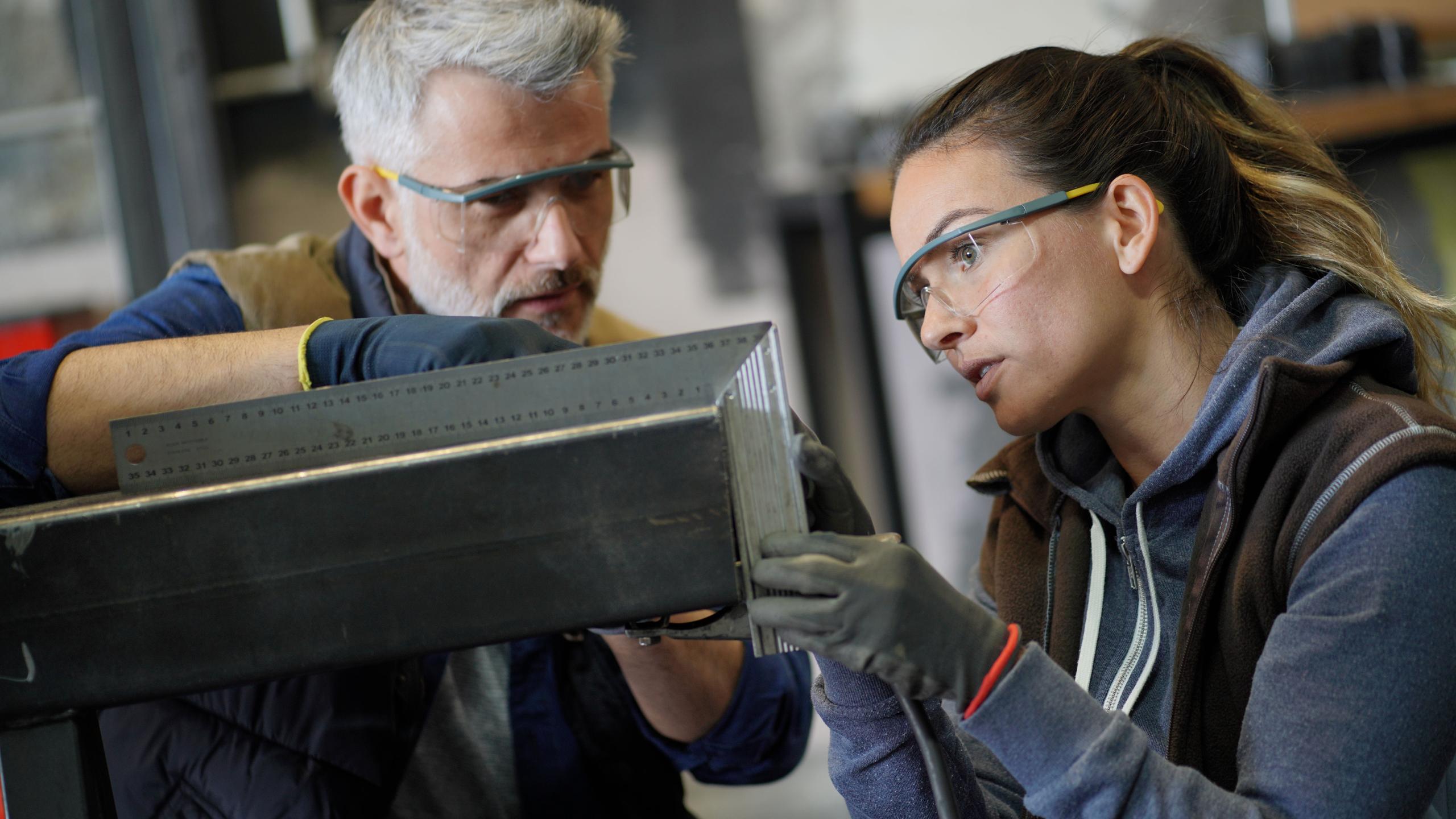 Leerkracht en studente werken met metalen onderdeel.