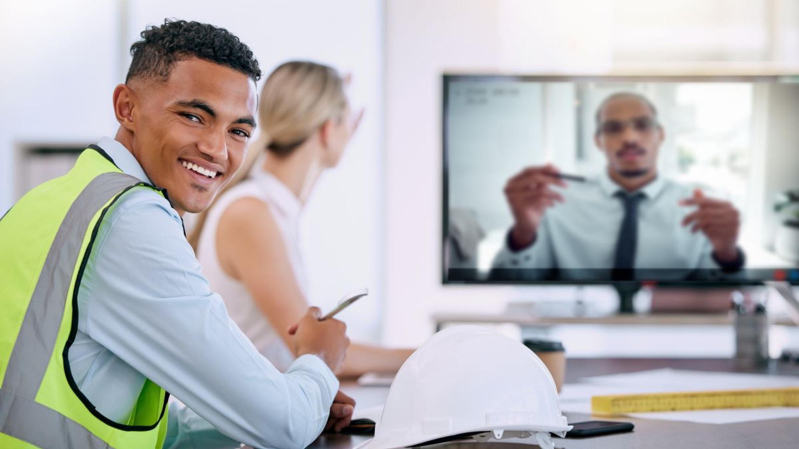 Jong man in fluohesje volgt opleiding met collega's via computerscherm.