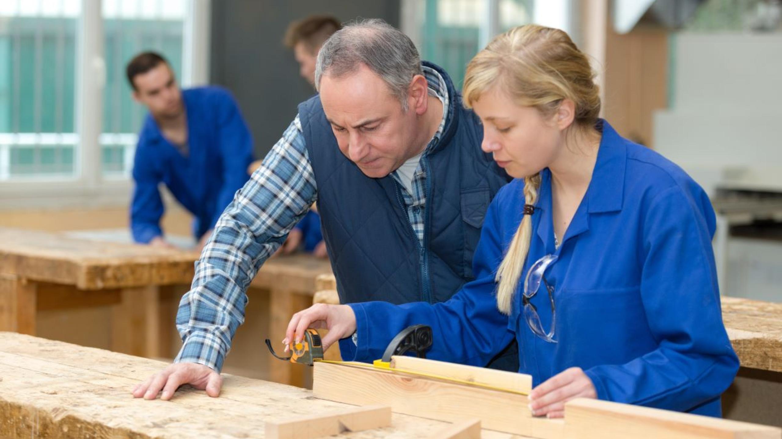 Leerkracht en leerling houtbewerking in atelier.