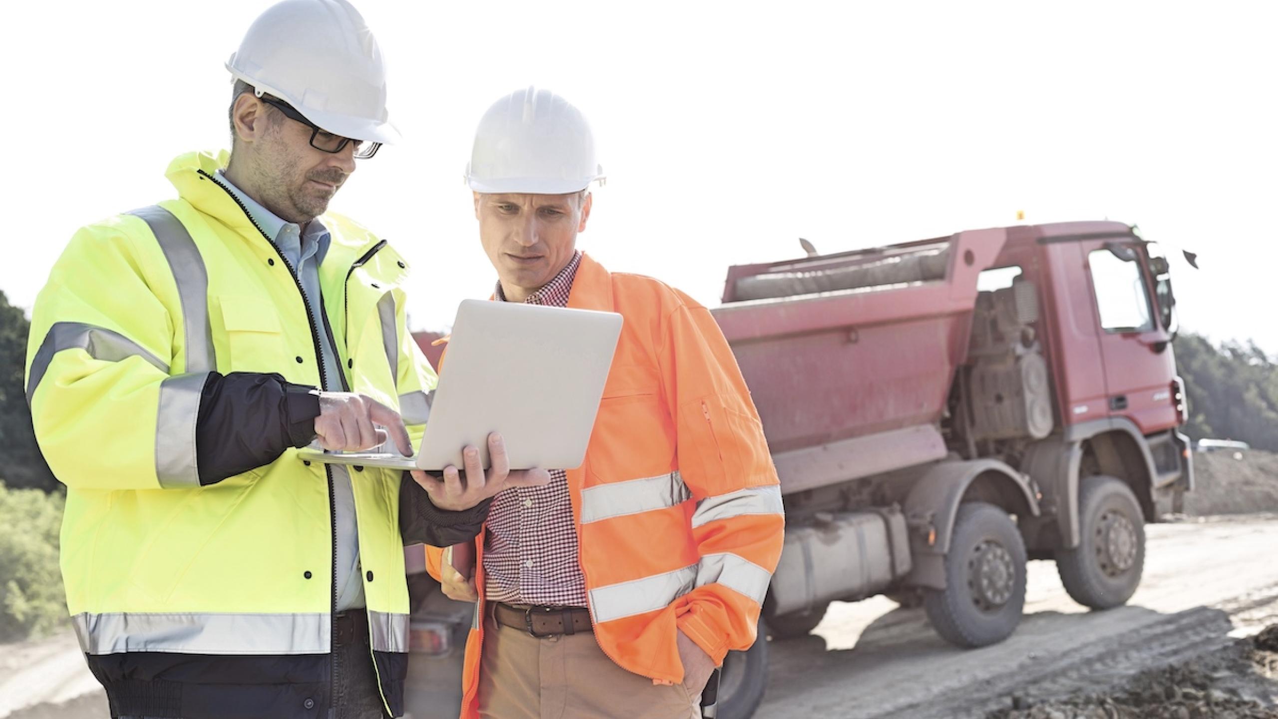 Twee mannen in fluohesjes met laptop op werf.